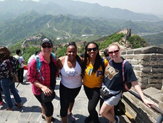 Four female students standing in front of the Great Wall of China.