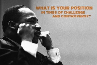 Photo of Dr. Martin Luther King Jr. with both of his arms raised and his fists clentched and the words What is your position in times of challenge and controversy?