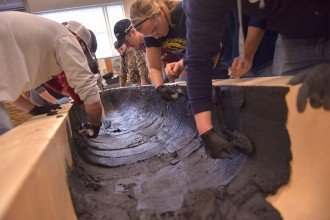 Concrete canoe team members lean over a Styrofoam mold and trowel on concrete.