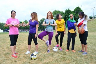 A group of women poses with athletic equipment, including a soccer ball, badminton racket and basketball.