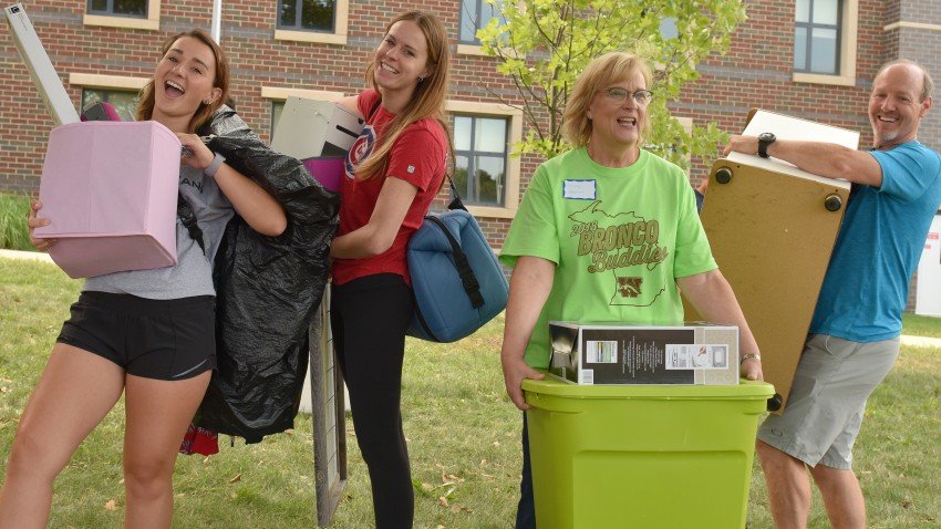 Two students and their helpers carry items into a residence hall.