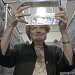A female scientist holding up a clear bin containing fish.