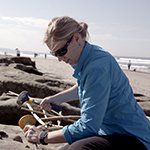 Female scientist at a beach excavating items from the sane.