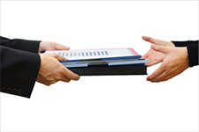 a set of hands handing another pair of hands a stack of papers