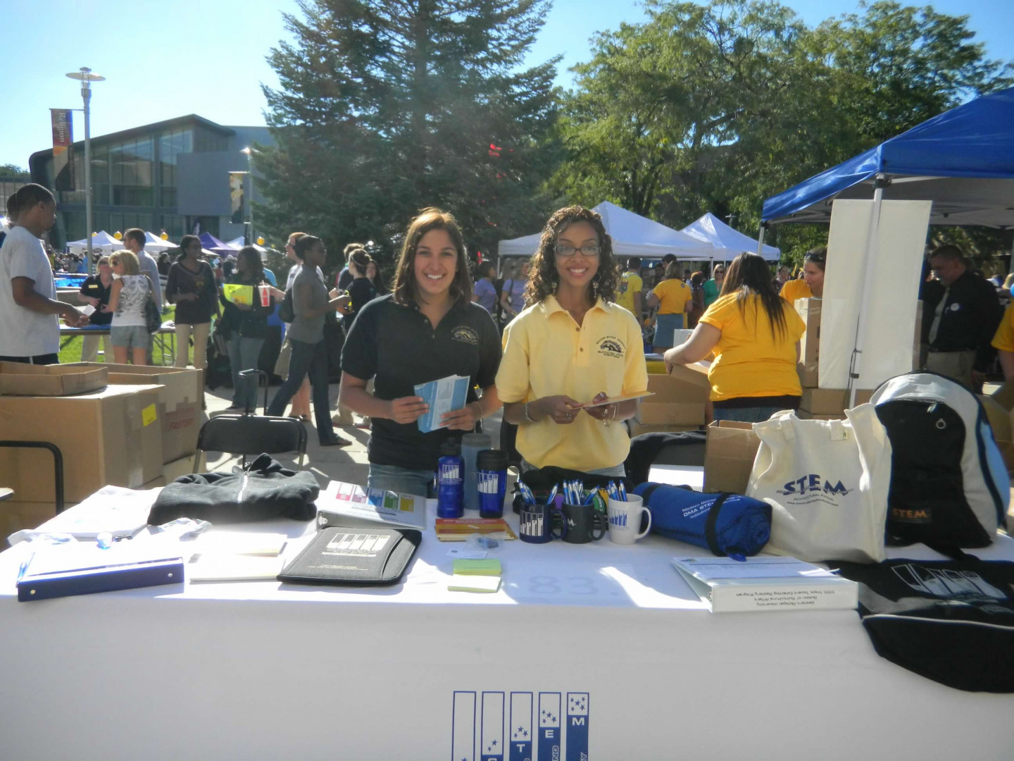 Two student employees standing behind a table with promotional items at Bronco Bash.