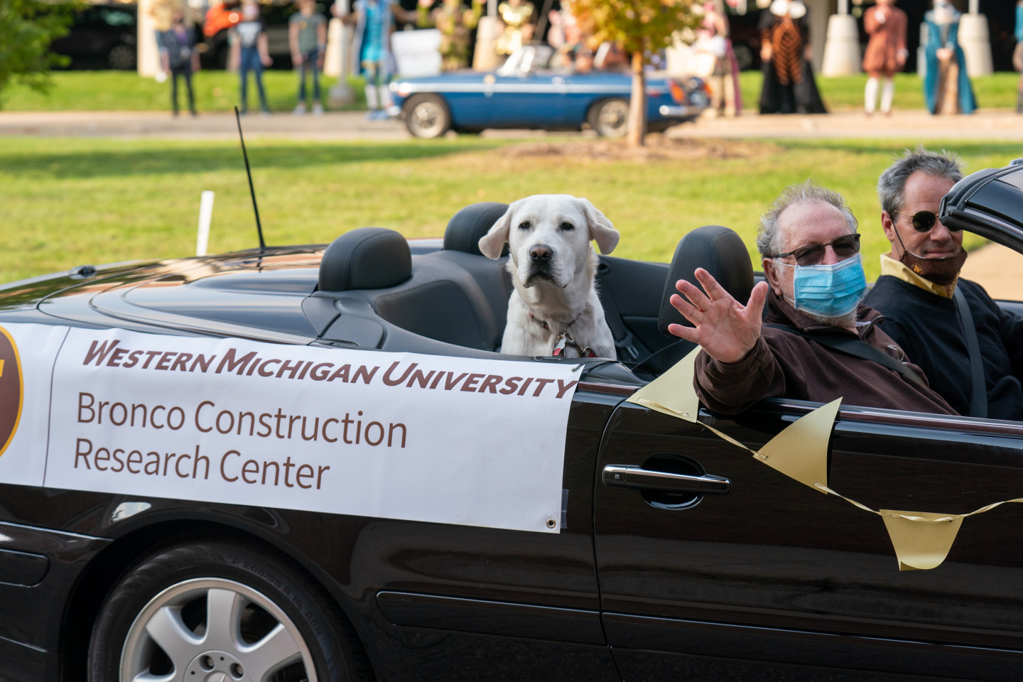 A dog sits in the back of a car with a "Bronco Construction Research Center" sign.