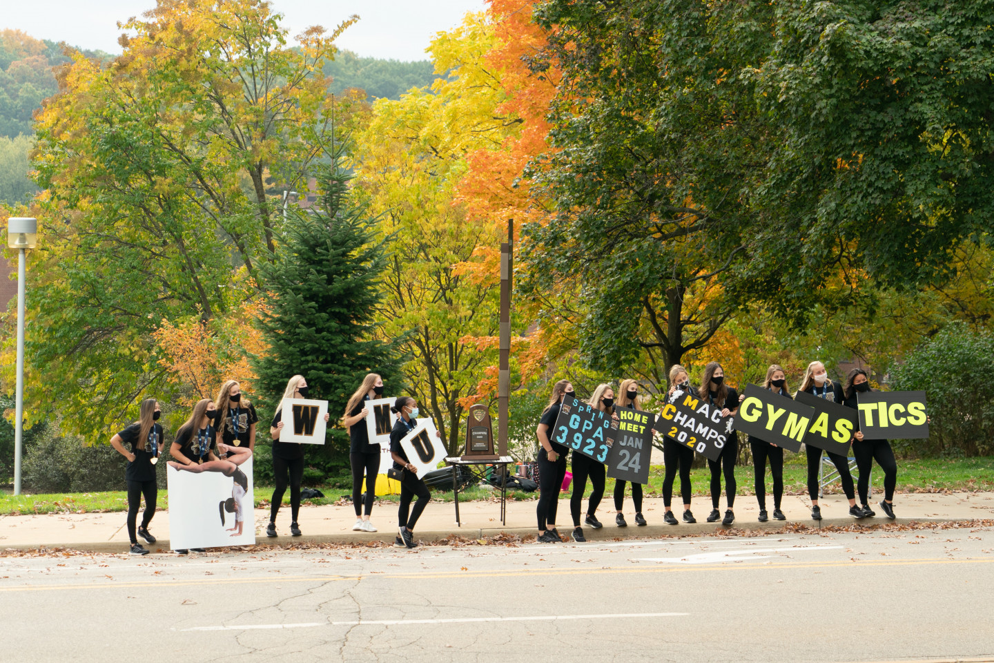 The WMU gymnastics team holds signs along the side of the road.