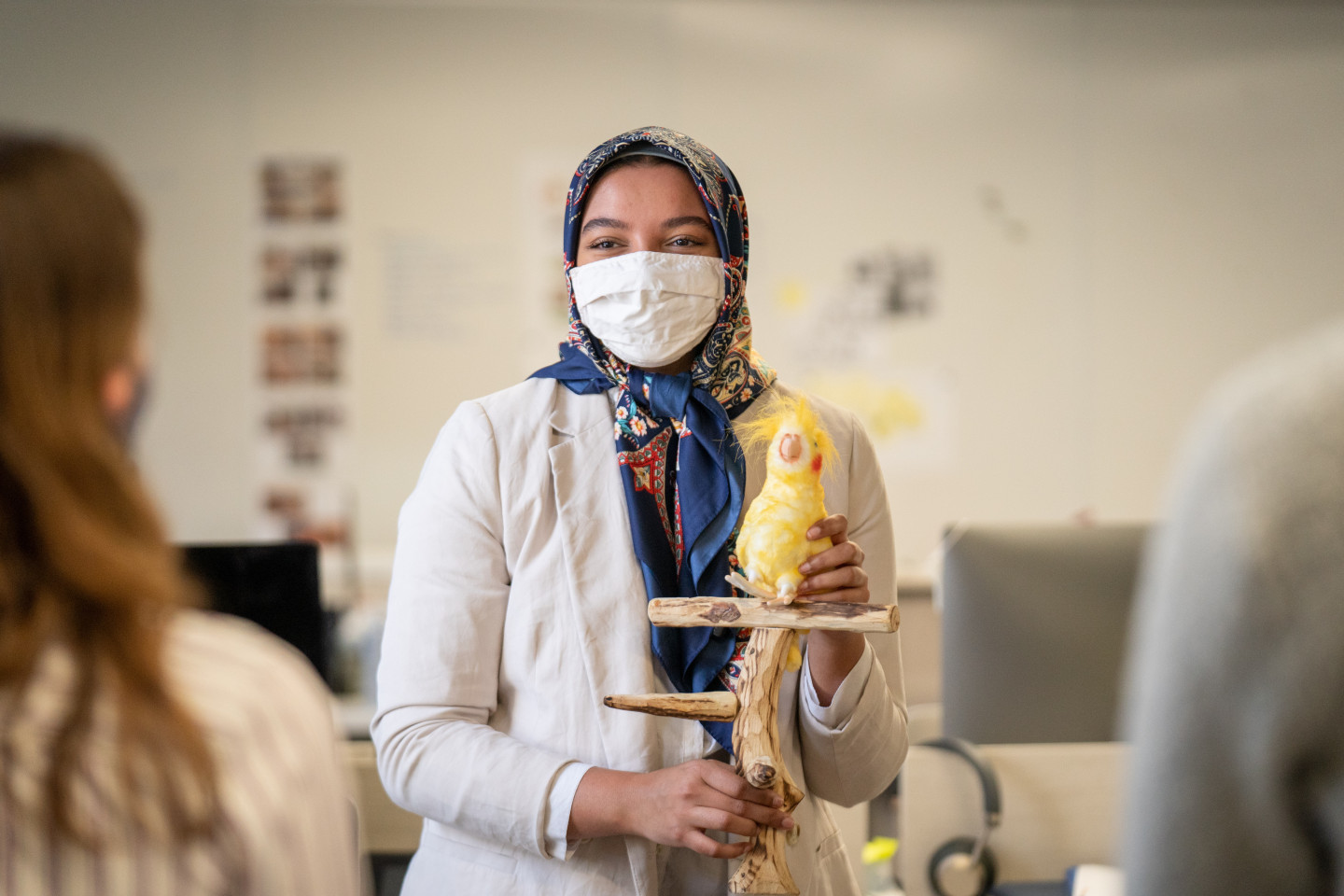 Aisha Thaj holds a stuffed animal bird on a perch she designed.