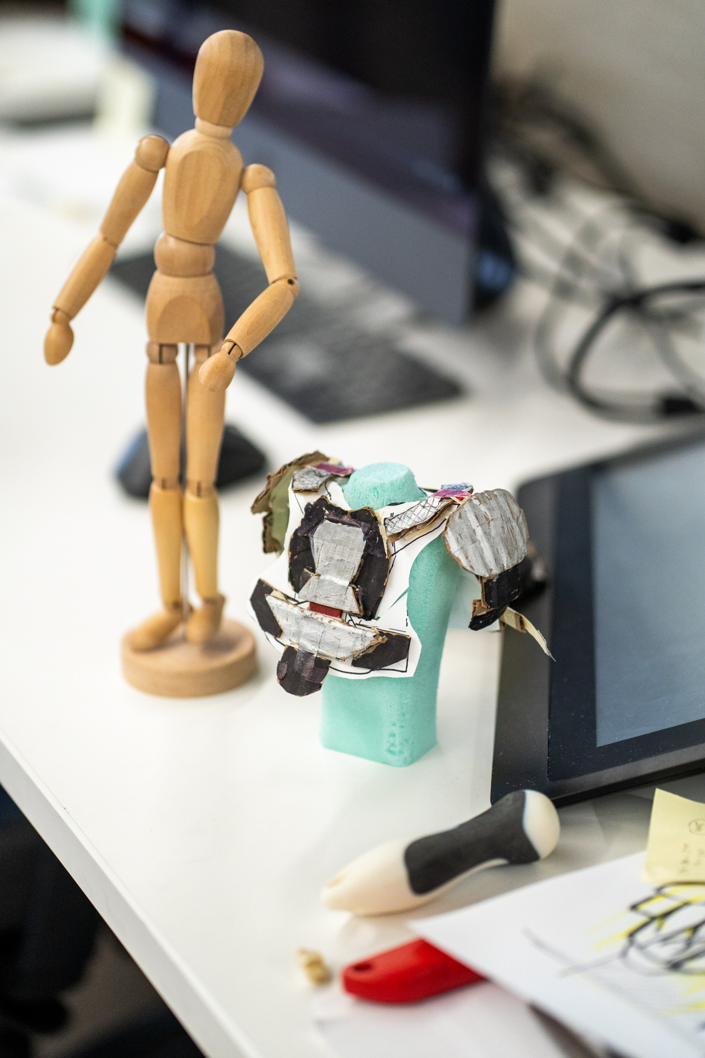 A small wooden sculpture stands next to a small paper design on a desk.