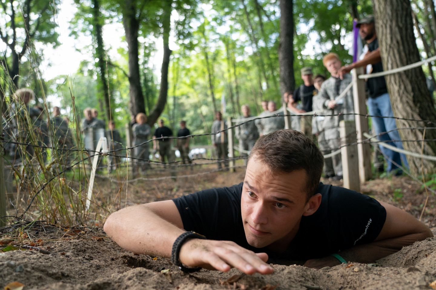 An ROTC cadet crawls under barbed wire on an obstacle course.