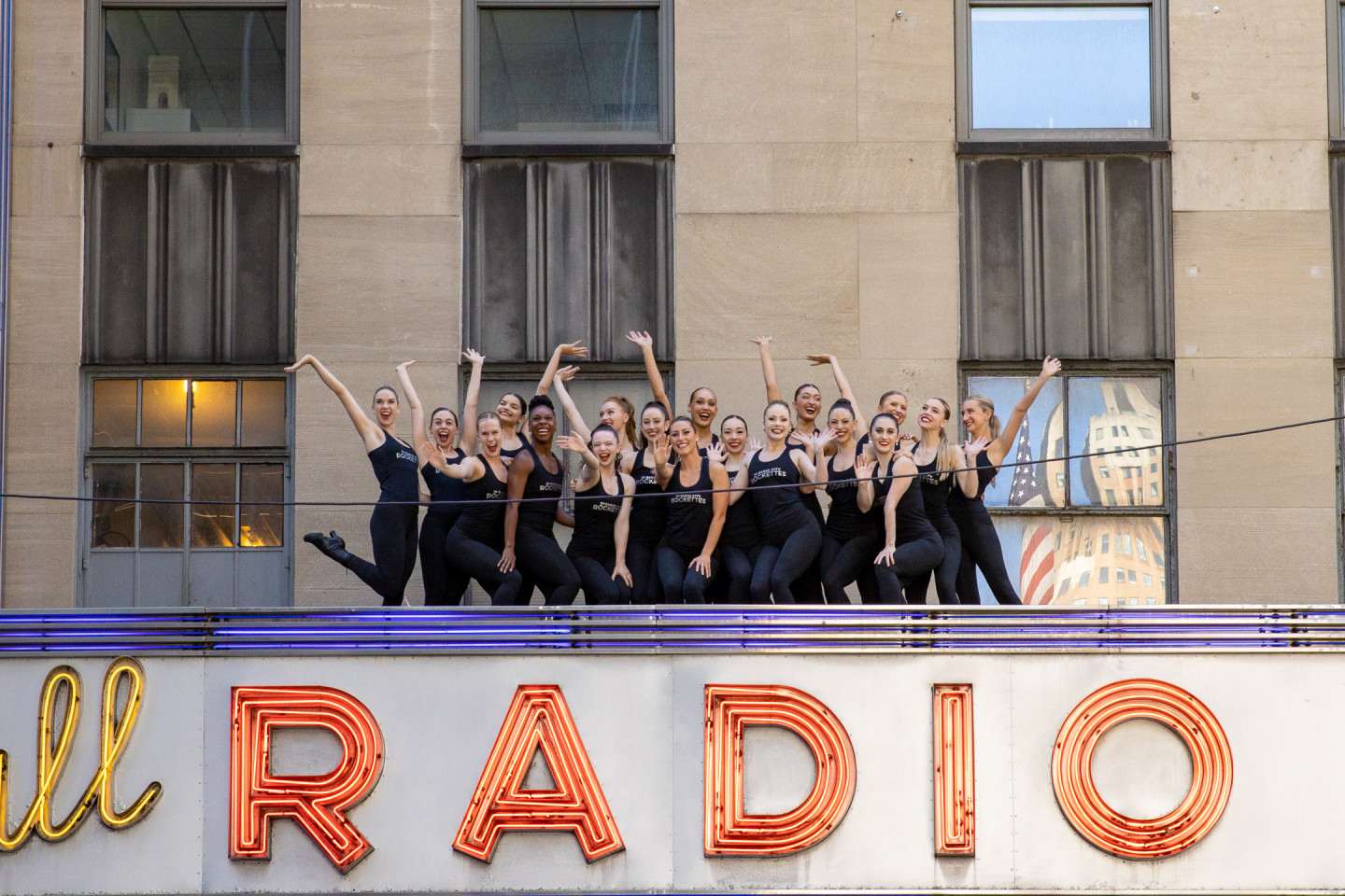 A group of dancers stands on the Radio City Music Hall marquee.