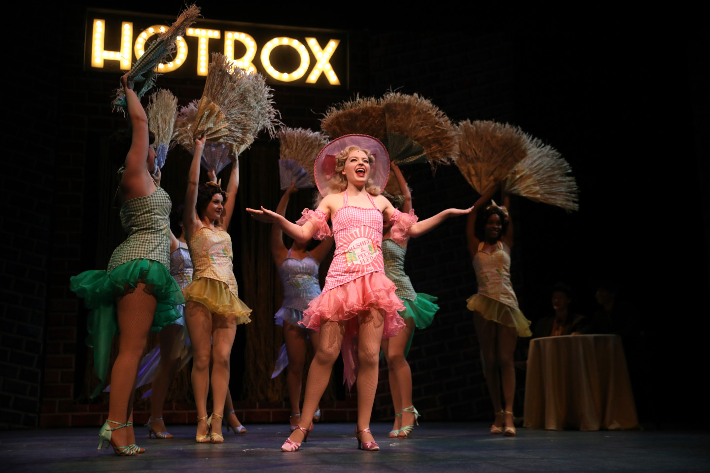 An actress in a pink dress dances at the Hotbox Club on stage in "Guys and Dolls."