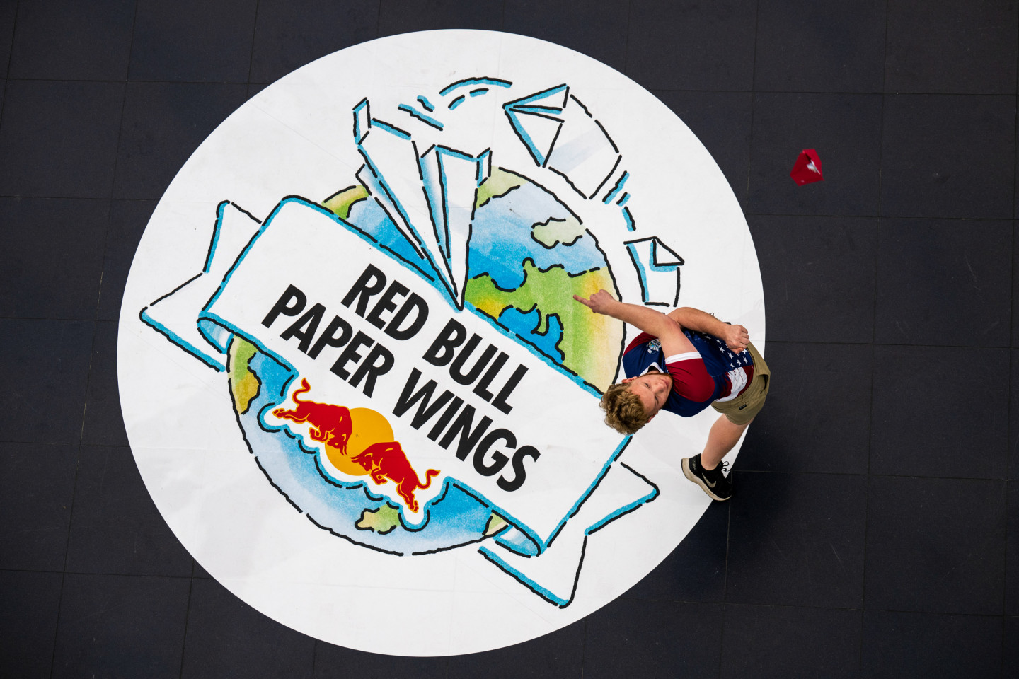 An aerial photo of Evin Cooper throwing a red paper airplane while standing on the "Red Bull Paper Wings" logo.