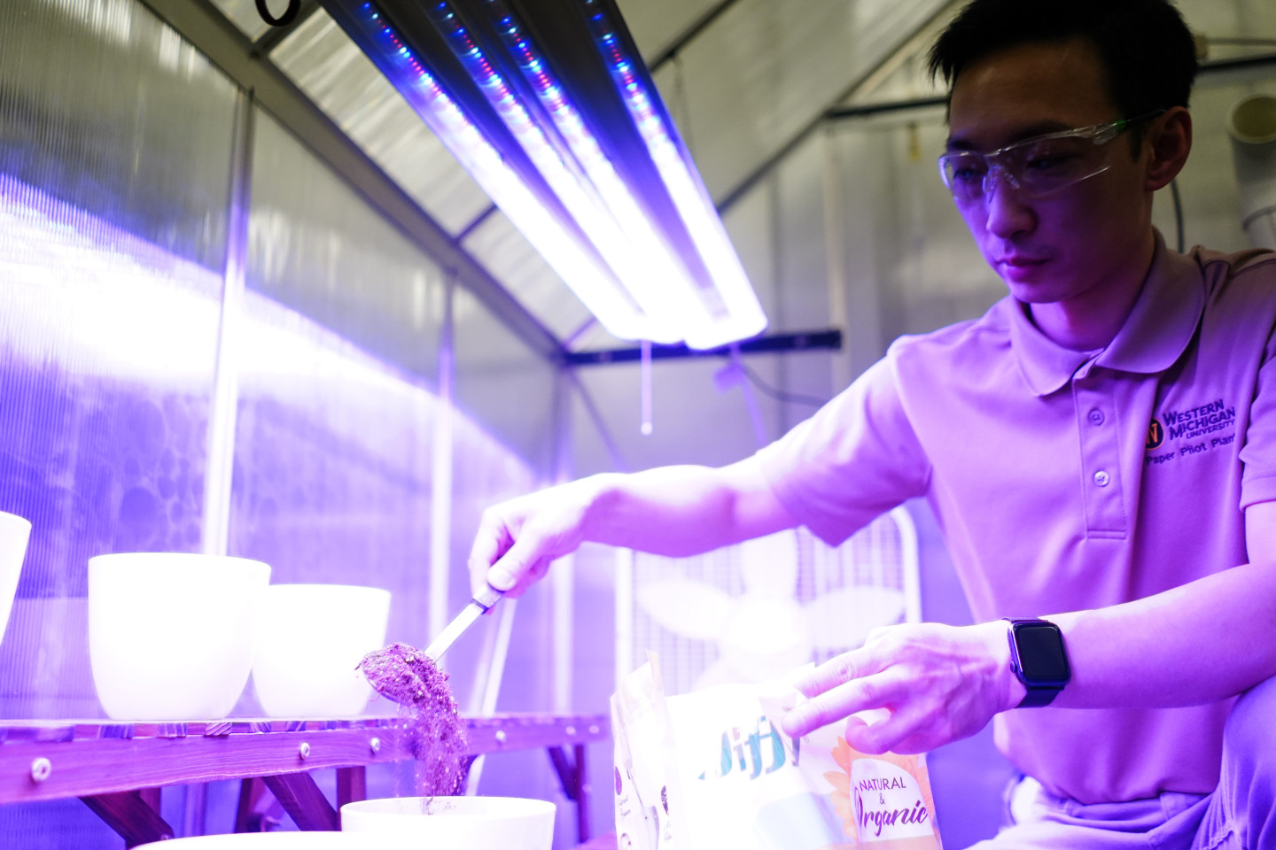 Jason Wang uses a large spoon to fill pots with soil.