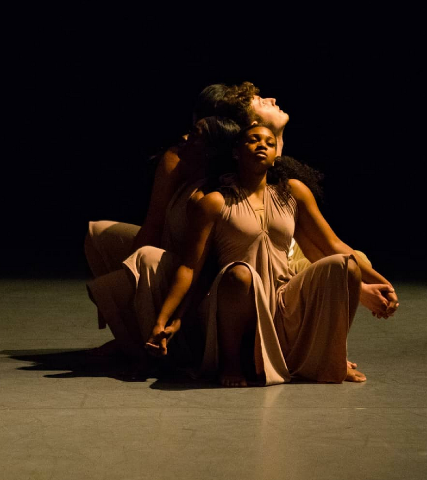 Dancers in nude dresses stand with their backs together.