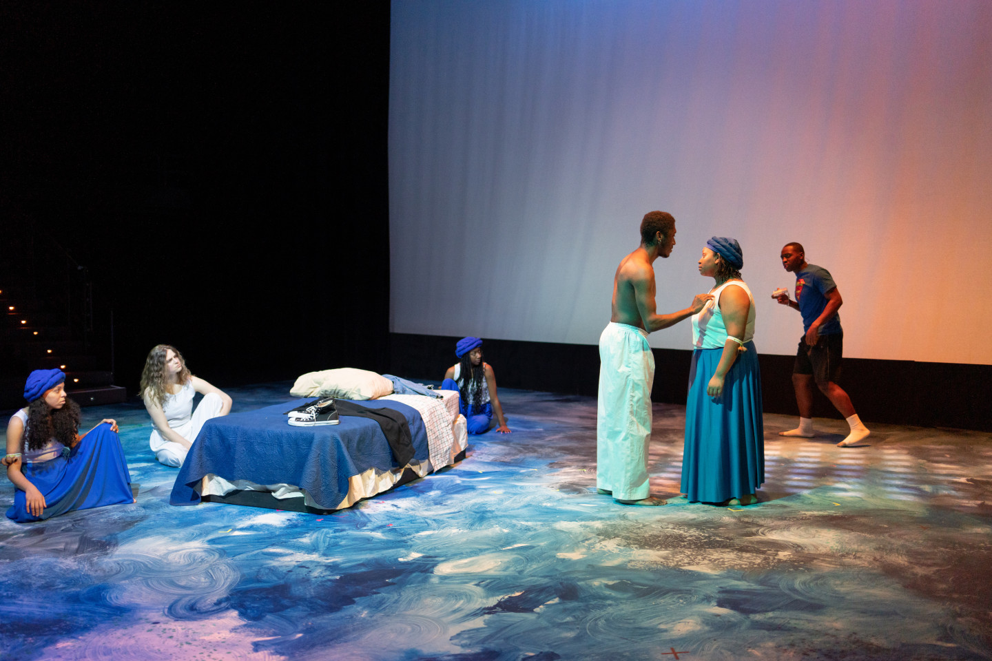 Actors perform on a stage filled with white and blue swirling colors.