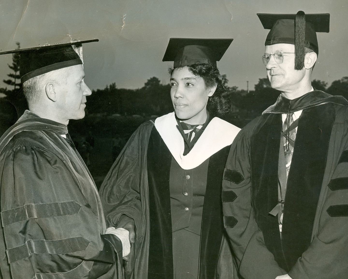A black and white photo of three people in graduation regalia.