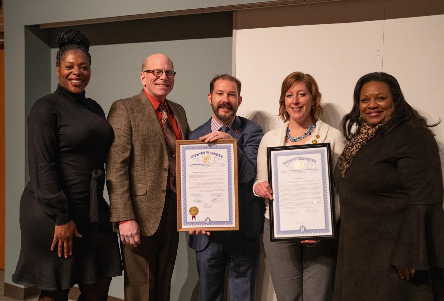 A group of people stand together displaying two framed certificates.