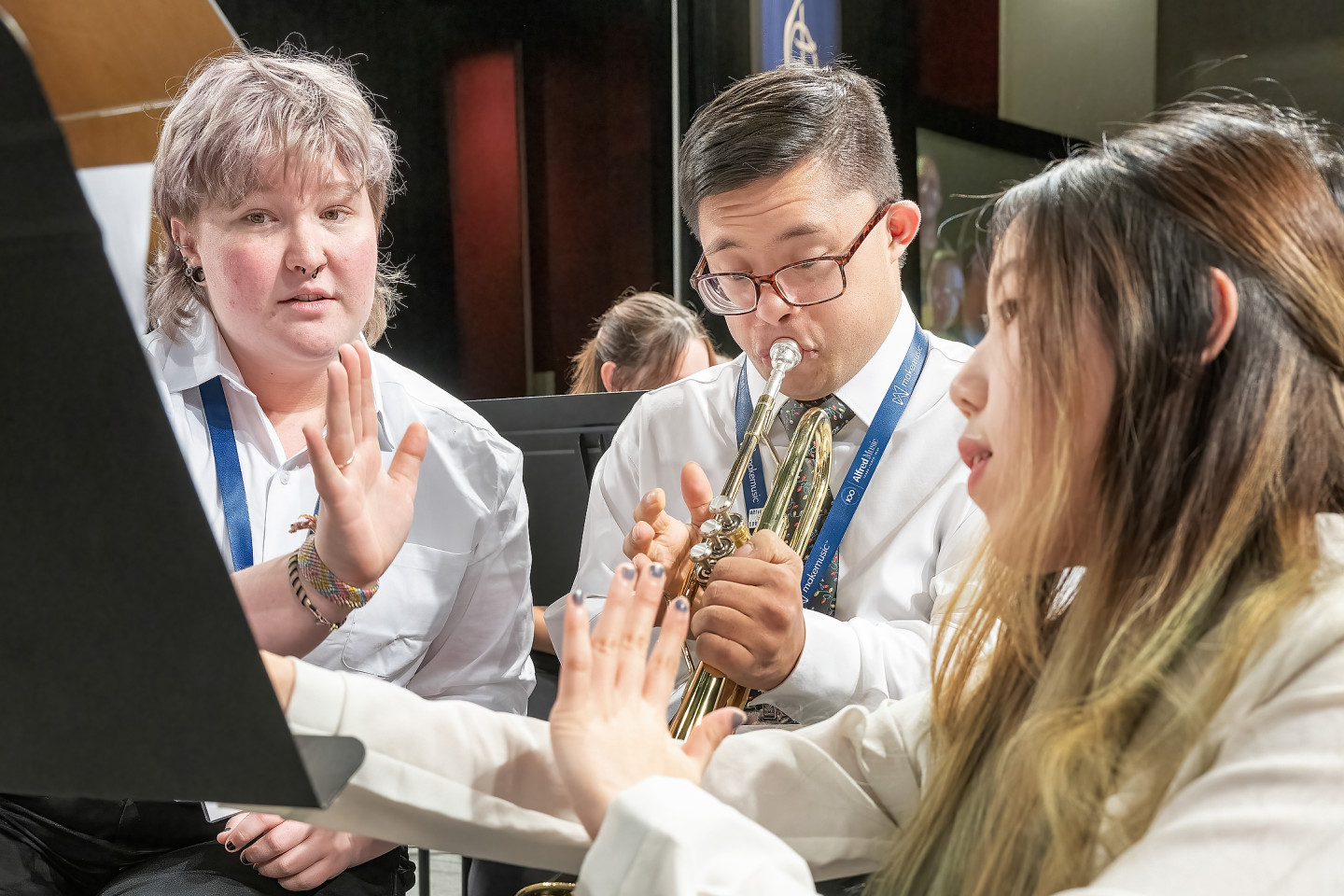 A musician plays a trumpet while two students hold up their hands to count measures.