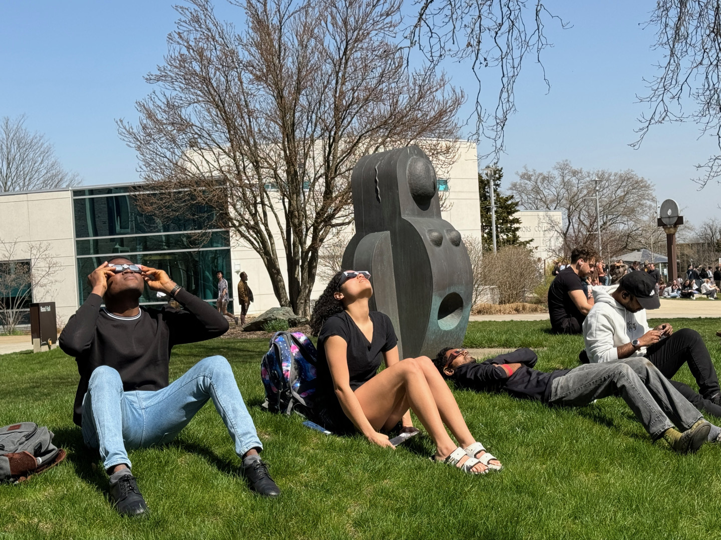 Students sit on the grass and look up at the sky.