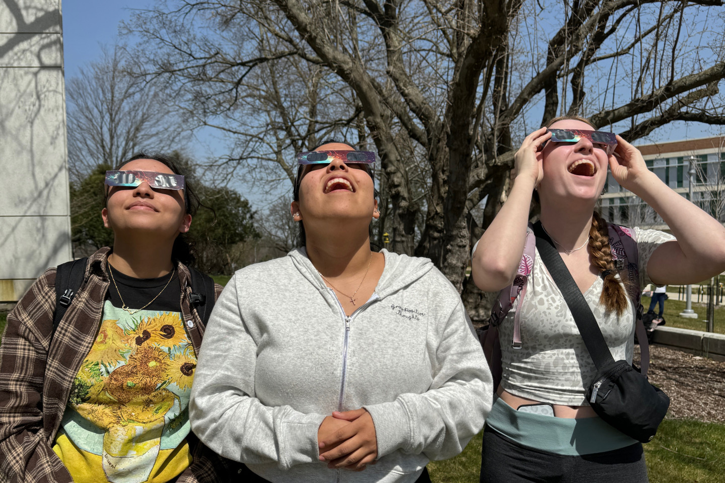 Three students wear eclipse glasses