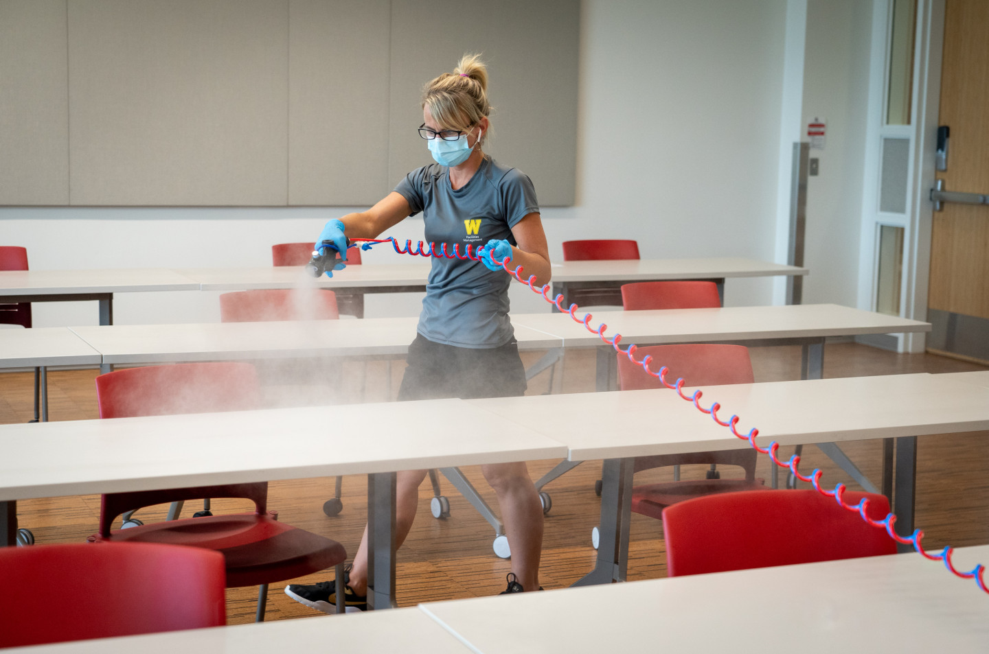 A WMU employee sprays disinfectant using a sprayer in a classroom.