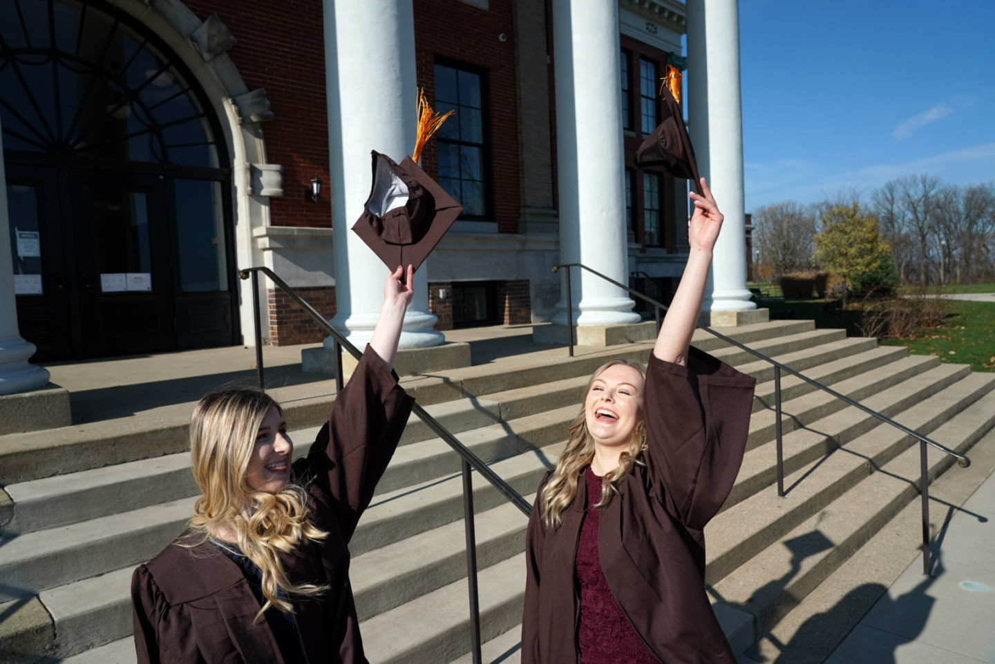 Two graduates wearing their gowns throw their caps into the air.