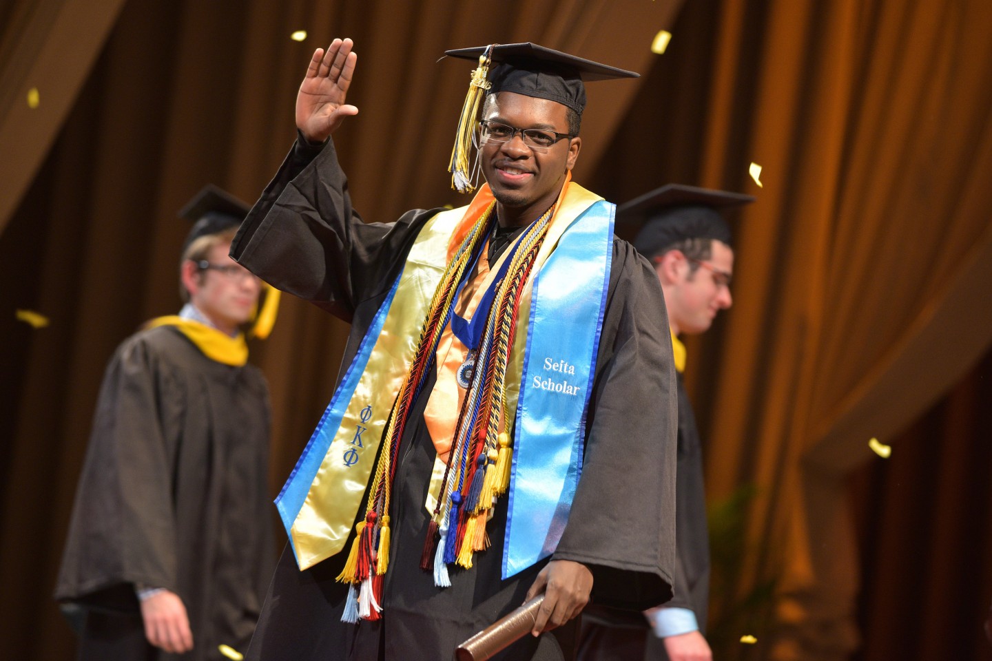 J. Gabriel Ware, dressed in his graduation regalia, waves at the camera after receiving his diploma.