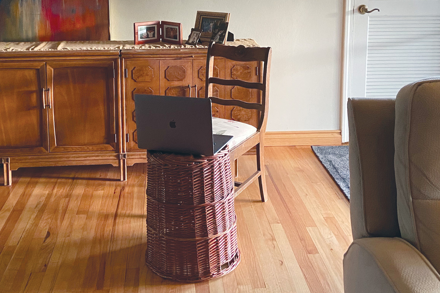 A laptop computer sits on an overturned laundry basket in a living room.