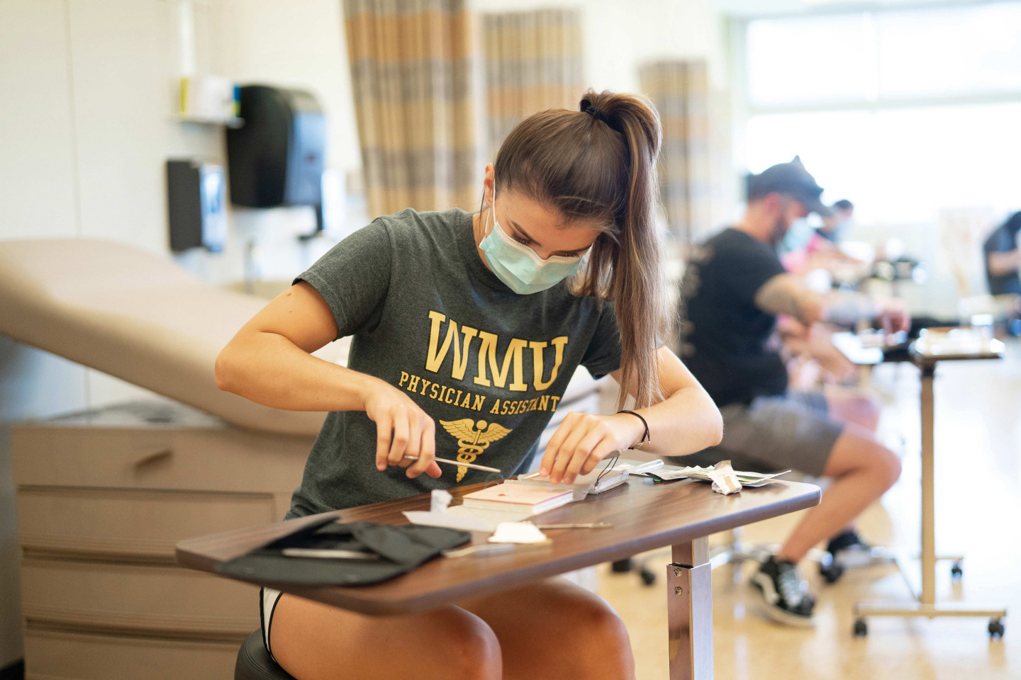 A physician assistant student sits at a desk and practices suturing.