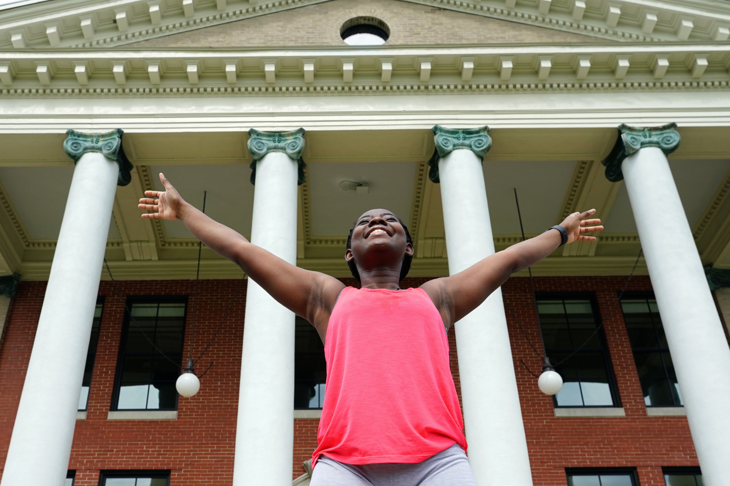 A student stands with her arms outstretched in front of Heritage Hall.