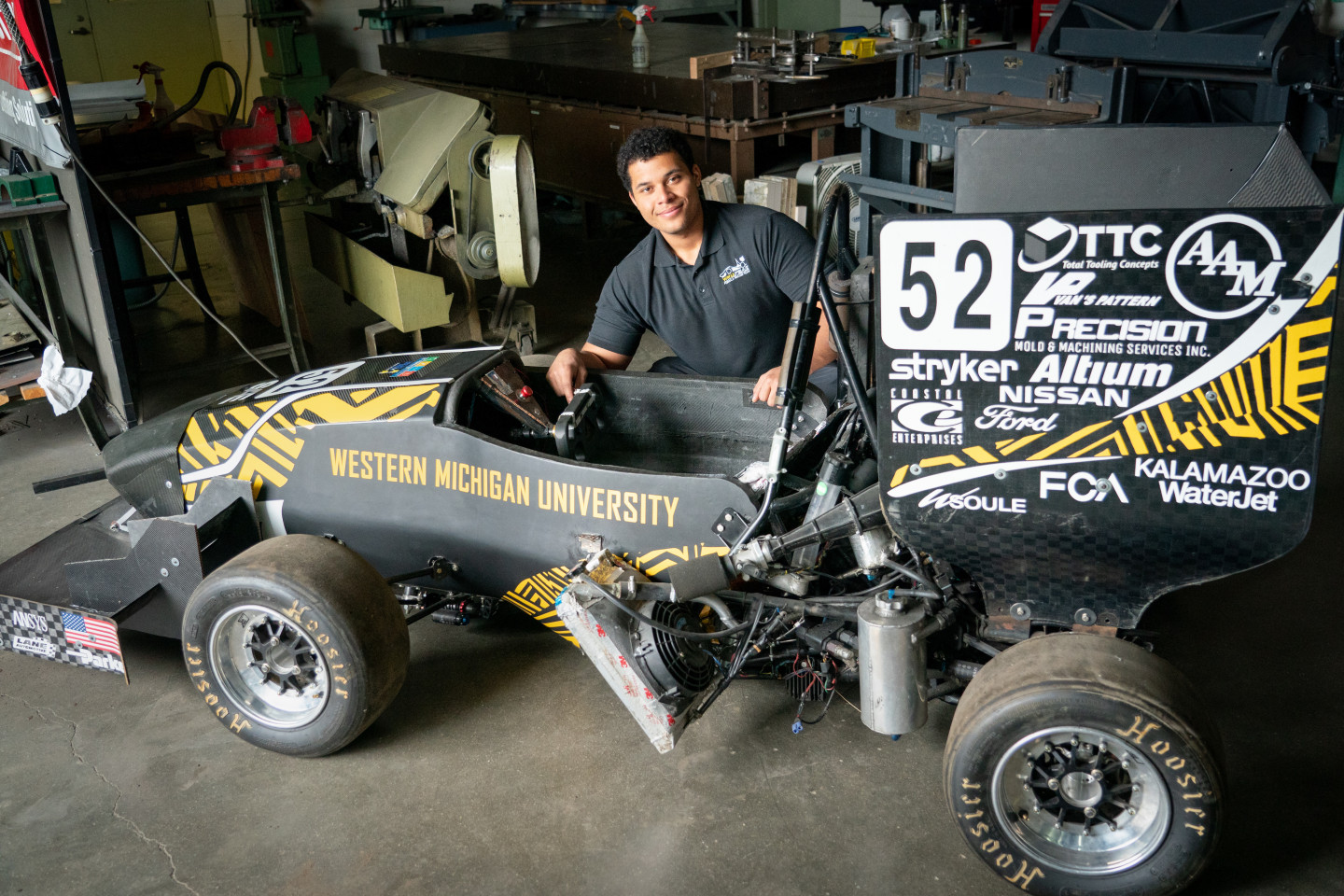 Nick Durham kneels next to a race car he helped build.