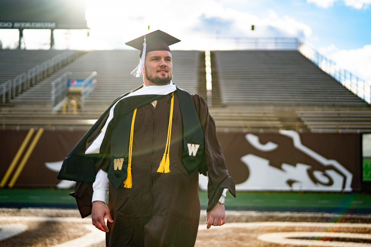 Mike Caliendo stands on the field in Waldo Stadium in his graduation cap and gown.