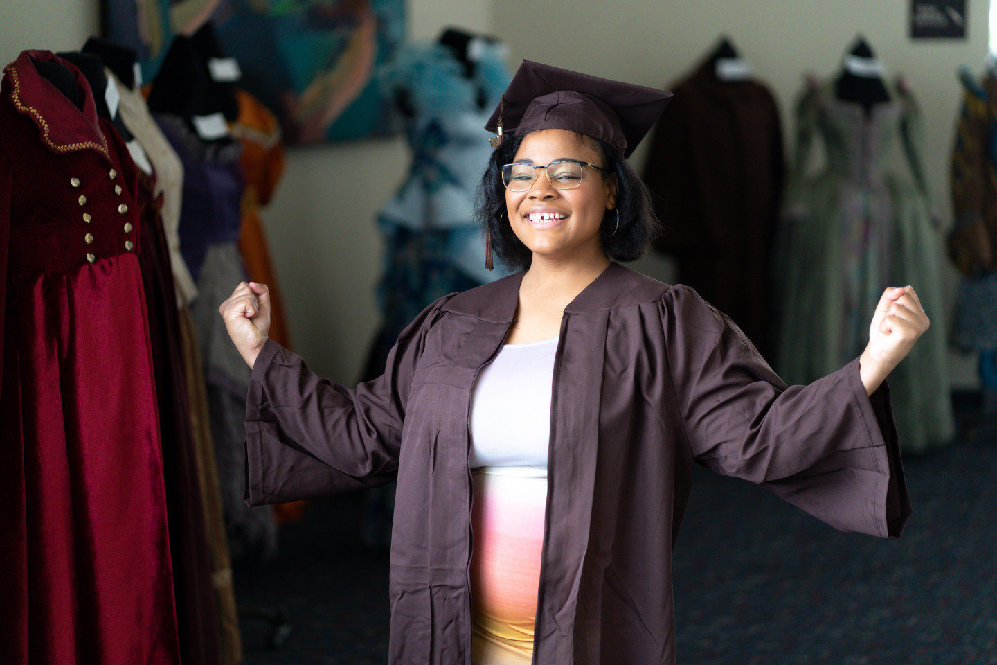 A photo of E.J. Taylor flexing her arms in her graduation attire.