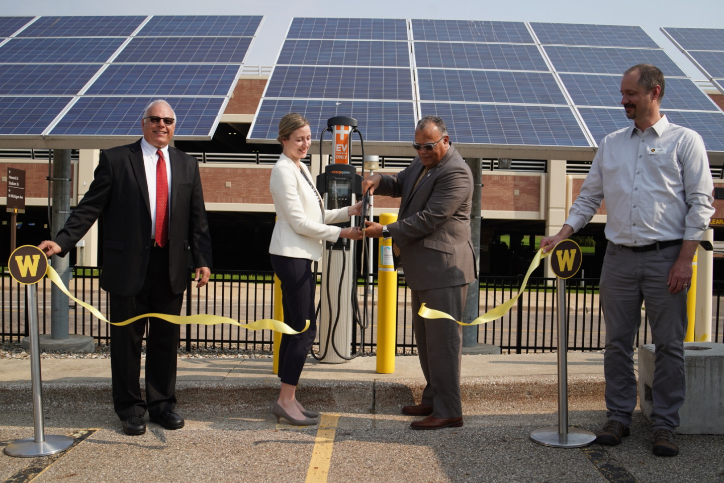 Western Michigan University leaders cut a ribbon in front of an electric vehicle charger.