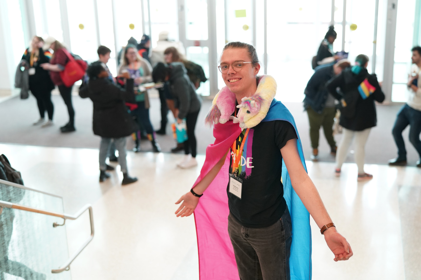 A student standing on stairs wearing the pansexual pride flag as a cape.