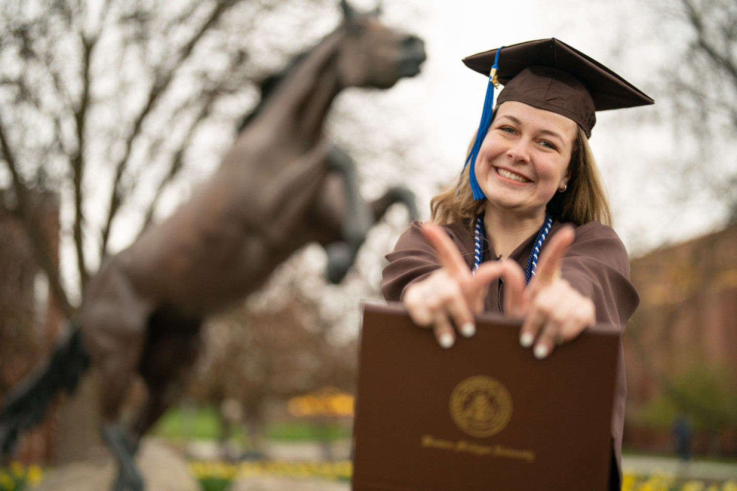 A Western graduate stands in her cap and gown holding her fingersin in the shape of a W.