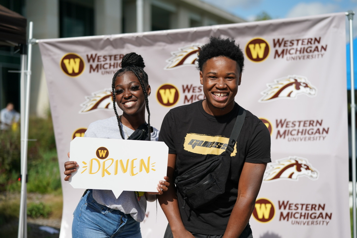 Students pose for a picture at Bronco Bash in front of a backdrop filled with Western Michigan University logos.