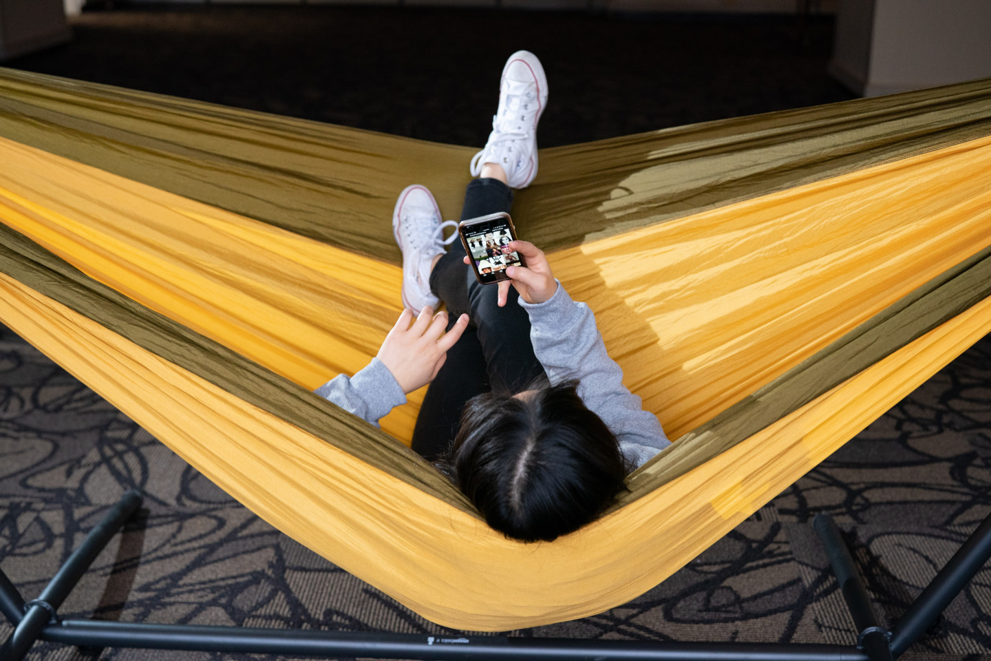 A student sits in a hammock looking at her phone.