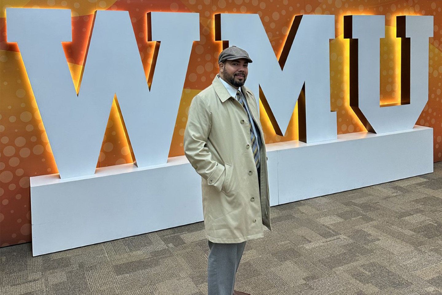 Julian Vasquez Heilig stands in front of an orange backdrop with WMU in large, white letters.