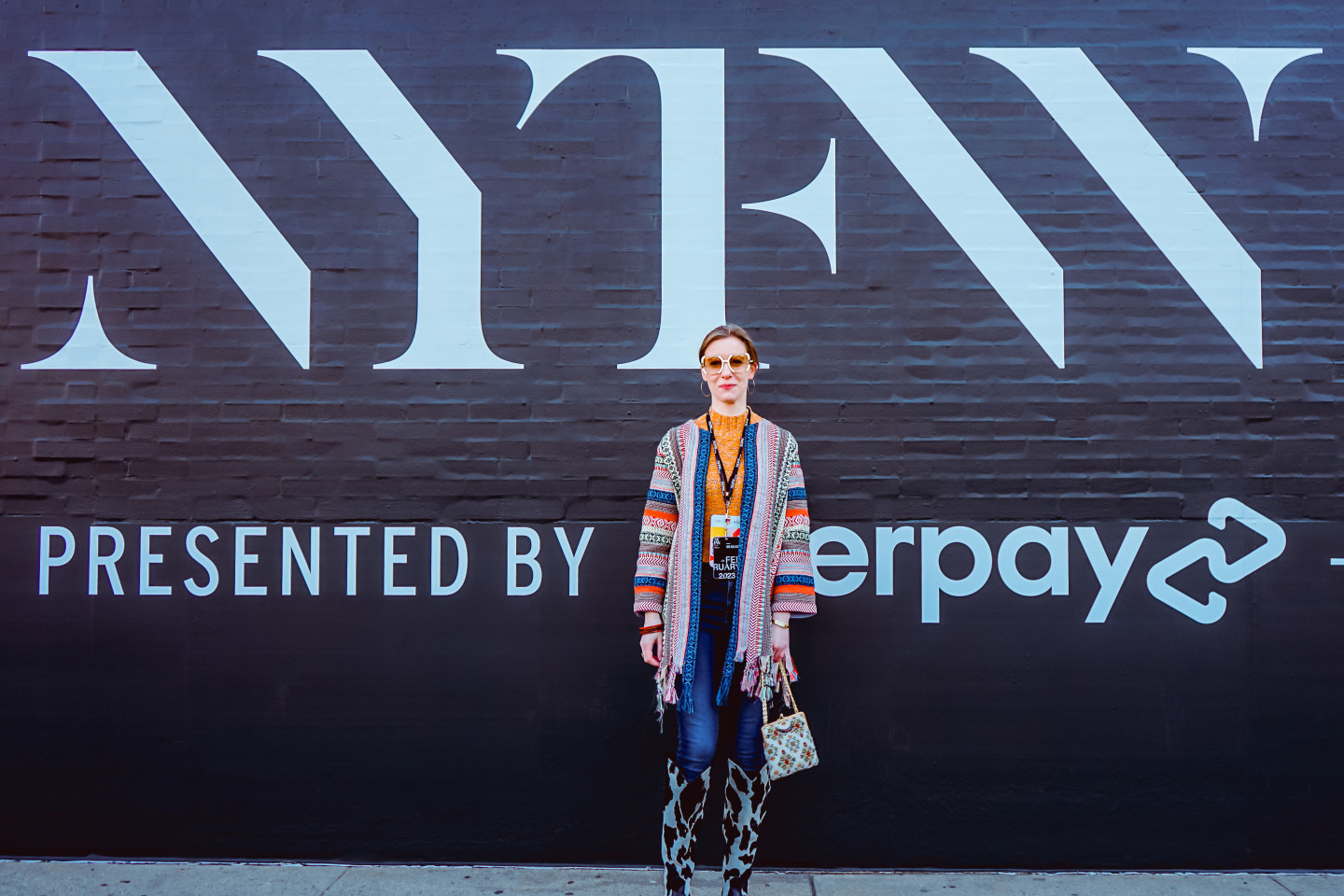 Julia LeKander stands in front of a black wall with white writing on it while attending New York Fashion Week.
