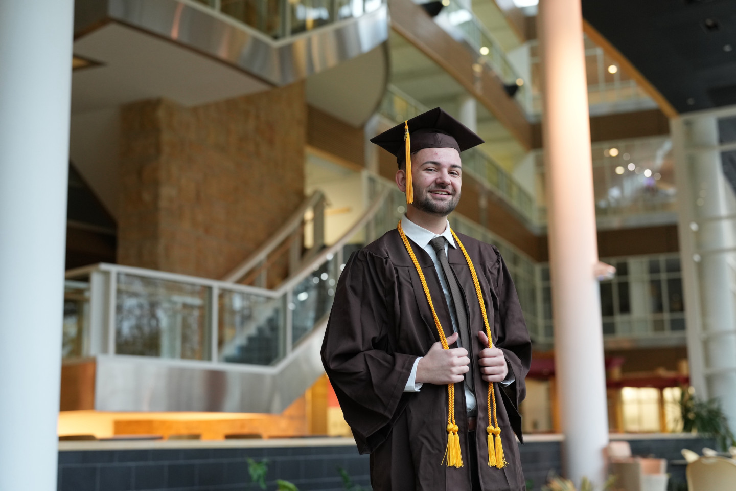 Cade Hine poses for a photo in his graduation cap and gown inside the atrium of the College of Health and Human Services building.