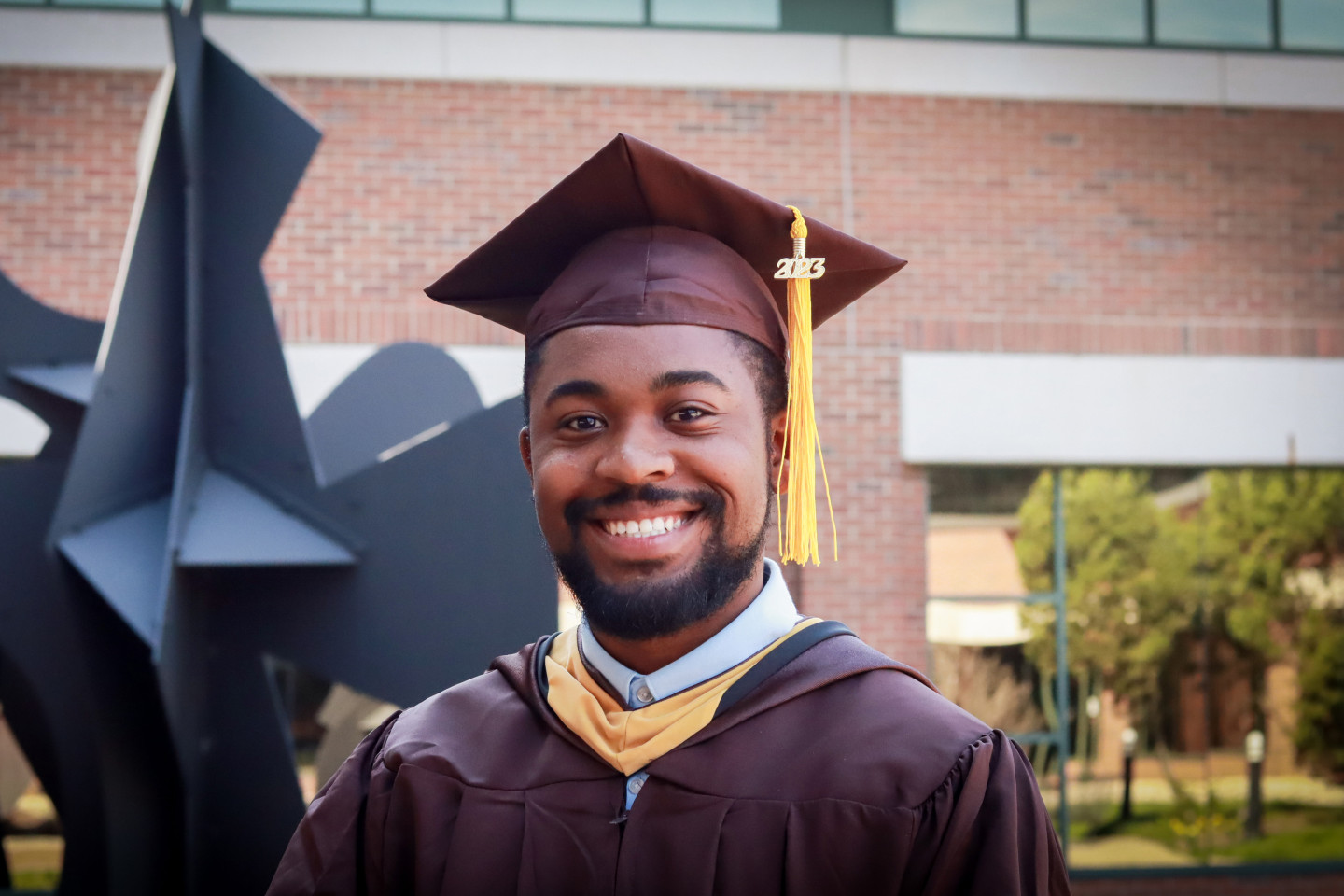Justin Scott smiles in his graduation cap and gown; a sculpture is in the background.
