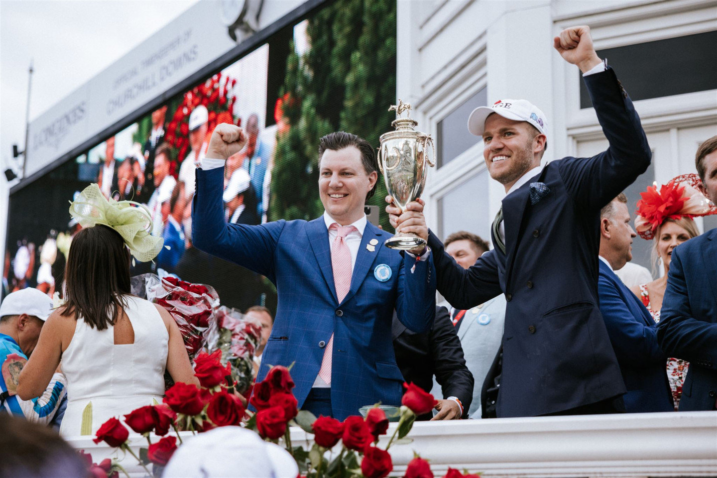 Brian Doxtator and Chase Chamberlin hold a golden trophy together while raising their fists into the air after the Kentucky Derby.