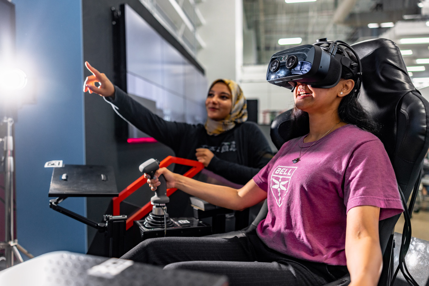 A girl wears a virtual reality headset while someone points at a screen in the background.
