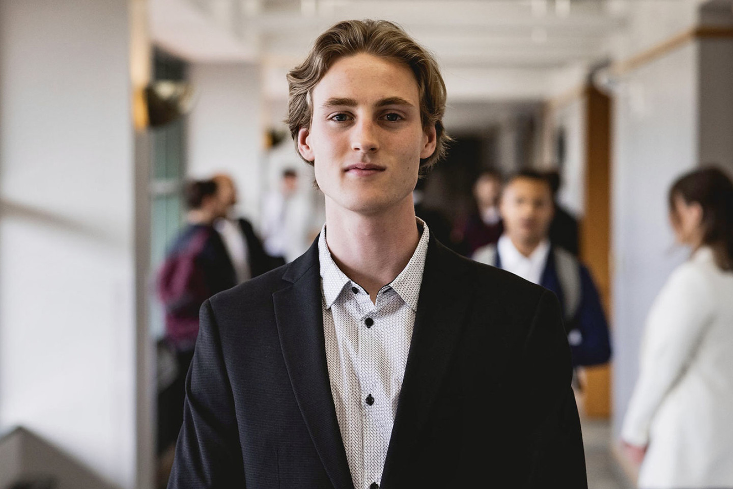 Photo of Eric Isaksson wearing a dark suit and standing in the hallway of Schneider Hall
