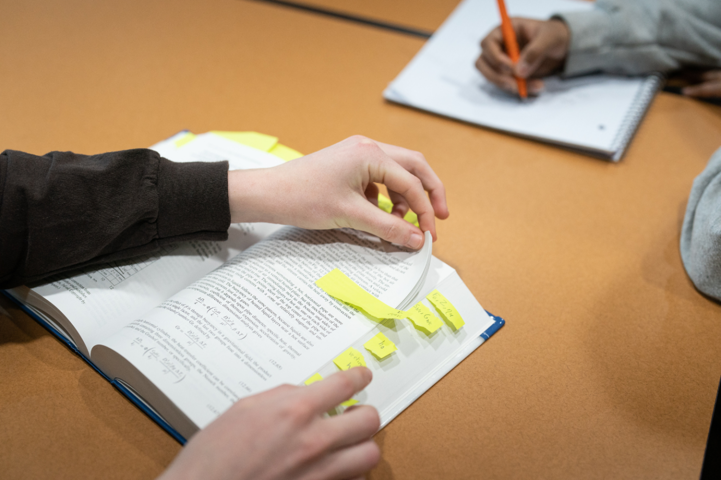 Student holding an open textbook with page markers.
