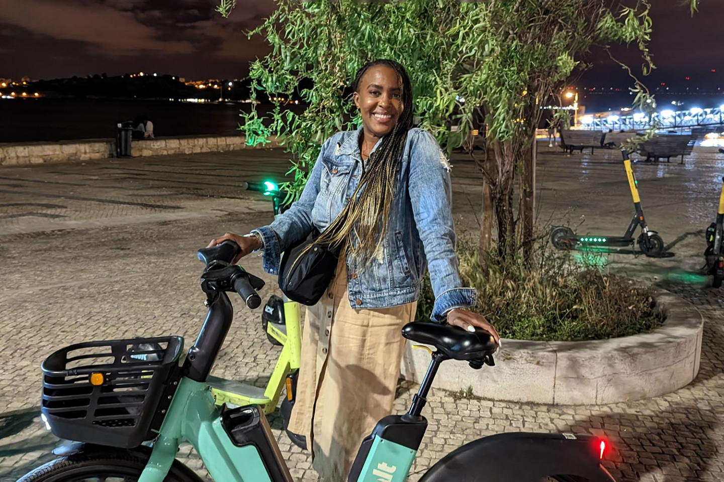 Syreeta Williams in Portugal, shown outside at night standing beside an electric bike