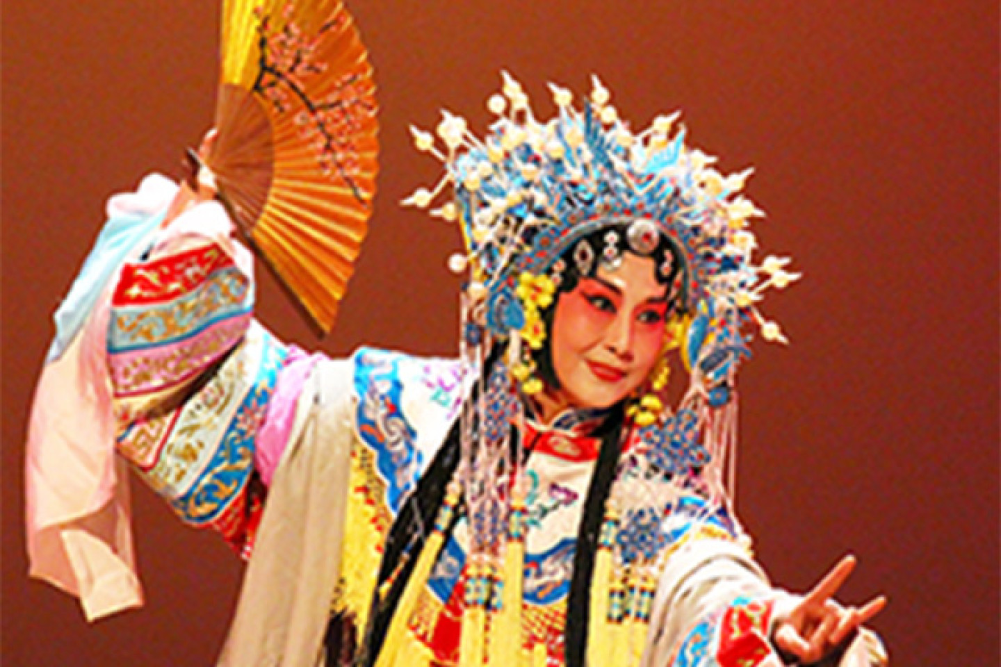 A Peking Opera dancer dressed in a colorful outfit holding a yellow fan.