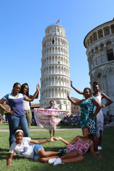 Seven girls pose in front of the Leaning Tower of Pisa.
